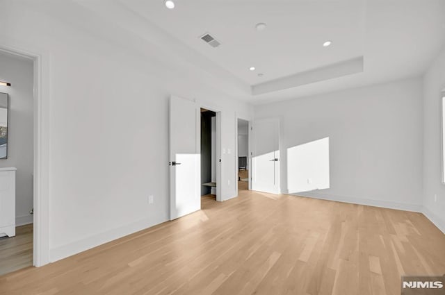 empty room with light hardwood / wood-style flooring and a tray ceiling