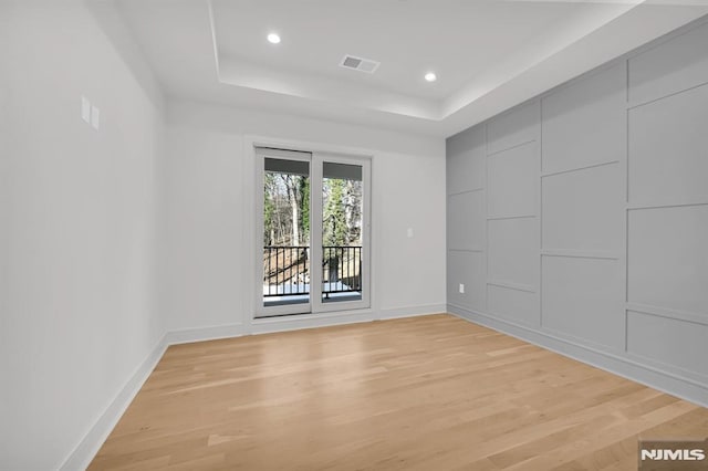 empty room with light hardwood / wood-style floors and a tray ceiling