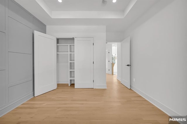 unfurnished bedroom with a raised ceiling and light hardwood / wood-style flooring