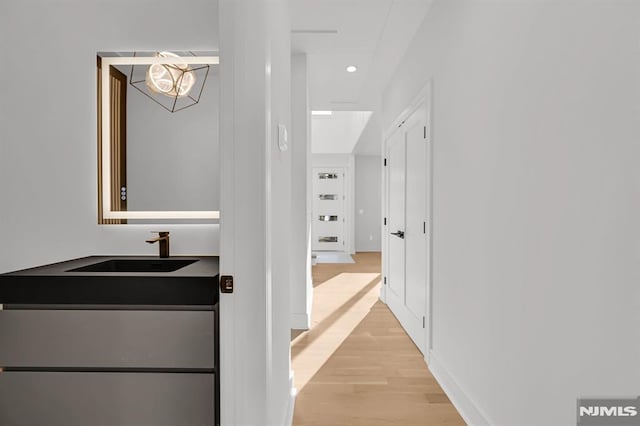 hall with sink, a chandelier, and light wood-type flooring