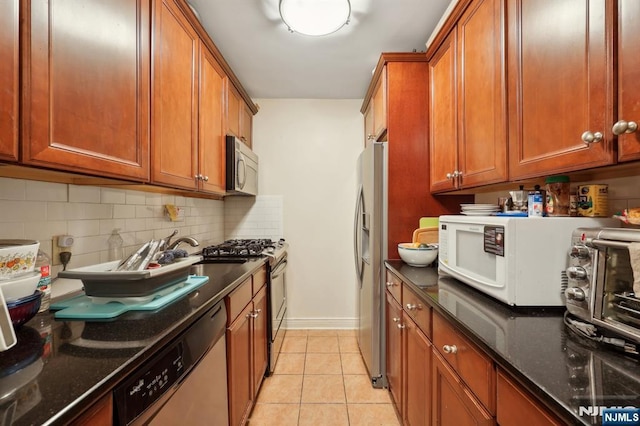 kitchen with brown cabinetry, light tile patterned floors, dark stone counters, and stainless steel appliances