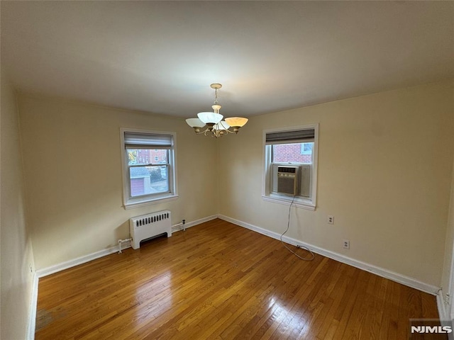 empty room featuring radiator, cooling unit, a chandelier, and hardwood / wood-style flooring