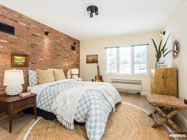 bedroom with brick wall, wood-type flooring, and radiator heating unit