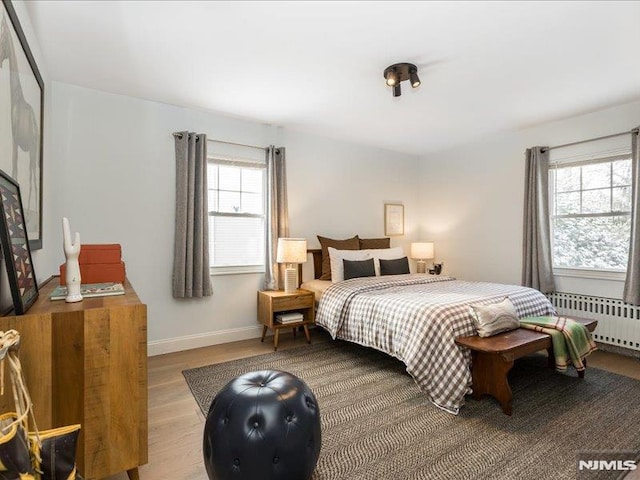 bedroom featuring multiple windows, radiator, and light hardwood / wood-style flooring