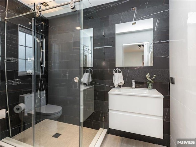 bathroom with toilet, a shower with door, decorative backsplash, tile walls, and vanity