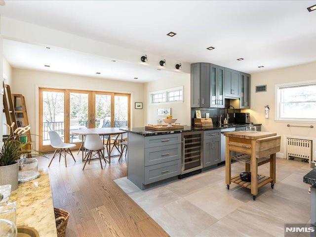 kitchen featuring wine cooler, gray cabinets, dishwashing machine, dark stone counters, and radiator heating unit