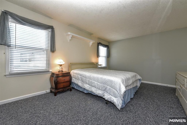 bedroom with a textured ceiling, dark carpet, and multiple windows