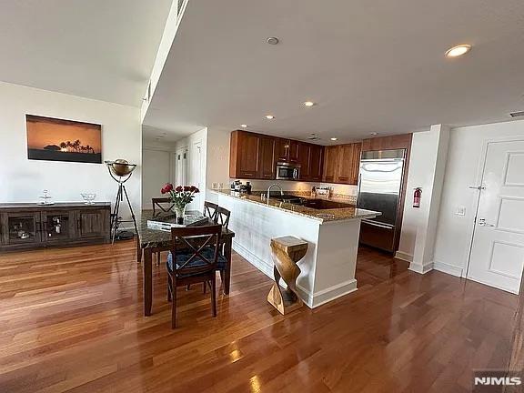 kitchen featuring kitchen peninsula, dark hardwood / wood-style flooring, stainless steel appliances, and dark stone counters