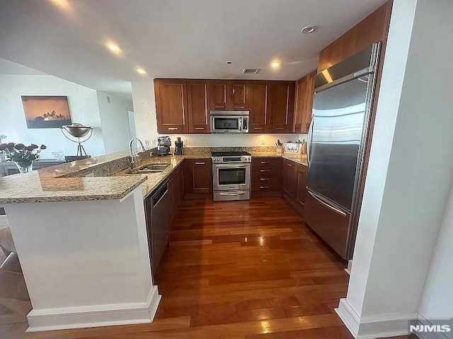 kitchen featuring light stone countertops, stainless steel appliances, sink, dark hardwood / wood-style floors, and kitchen peninsula