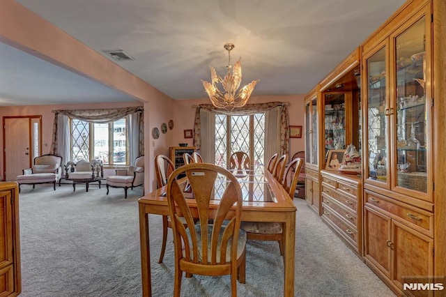 dining area featuring light colored carpet, plenty of natural light, and a notable chandelier