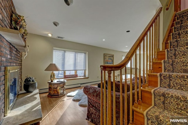 stairs featuring a brick fireplace, a baseboard radiator, and wood-type flooring