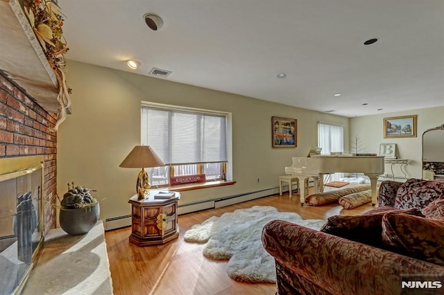 living room featuring a brick fireplace, plenty of natural light, baseboard heating, and light wood-type flooring