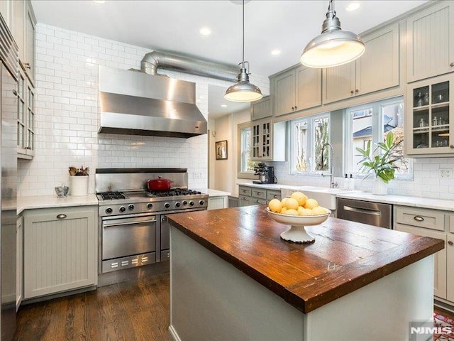 kitchen featuring butcher block counters, appliances with stainless steel finishes, wall chimney range hood, a kitchen island, and pendant lighting