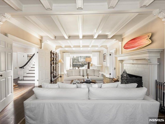 living room featuring a brick fireplace, dark wood-type flooring, ornamental molding, and beam ceiling