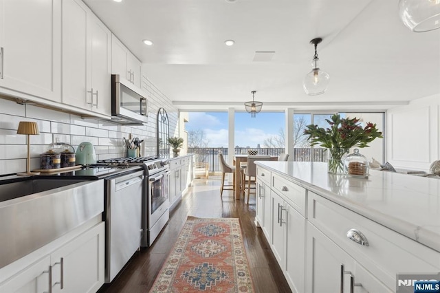 kitchen featuring pendant lighting, white cabinetry, decorative backsplash, light stone counters, and stainless steel appliances