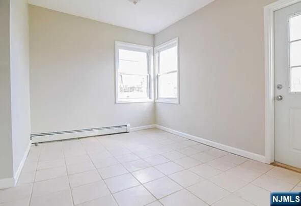 tiled empty room with a baseboard heating unit