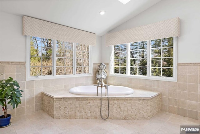 bathroom featuring vaulted ceiling, tile walls, and tiled tub