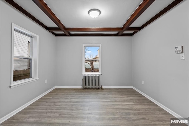 empty room with light hardwood / wood-style floors, radiator, beamed ceiling, and coffered ceiling