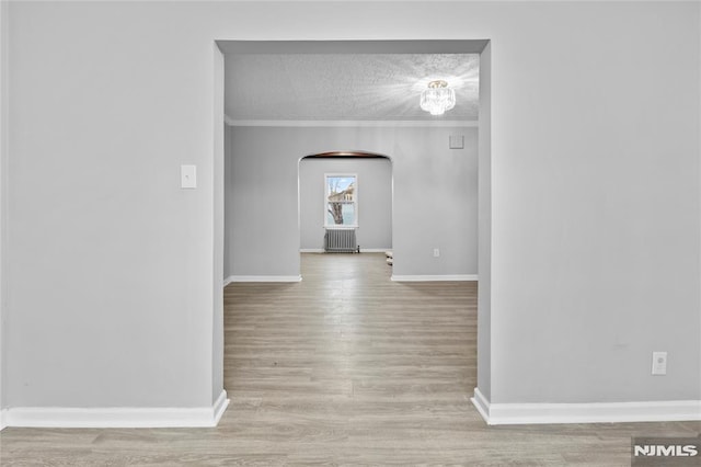 interior space featuring a textured ceiling, radiator, light hardwood / wood-style flooring, and ornamental molding