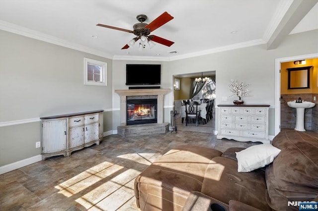 living room featuring visible vents, baseboards, a glass covered fireplace, crown molding, and ceiling fan with notable chandelier