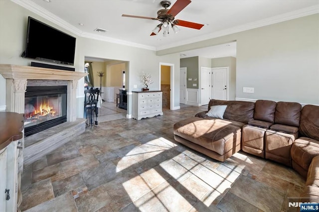 living room featuring a glass covered fireplace, crown molding, visible vents, and stone finish flooring