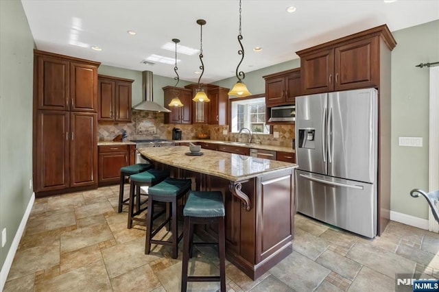 kitchen featuring decorative backsplash, appliances with stainless steel finishes, wall chimney exhaust hood, and stone tile floors