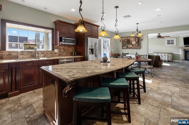 kitchen featuring stone tile floors, a sink, stainless steel appliances, backsplash, and a center island