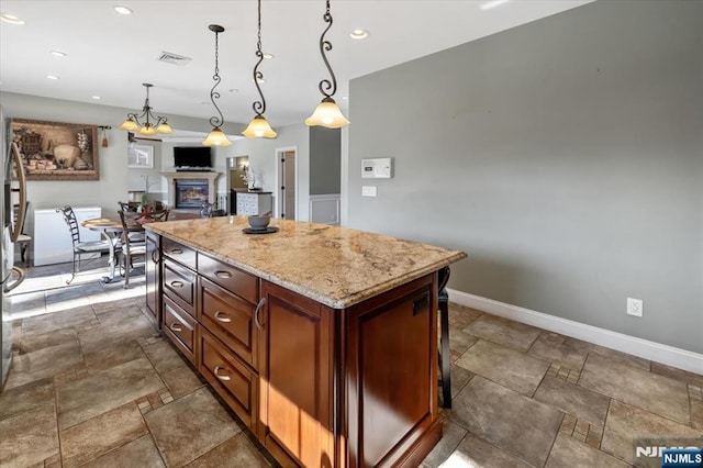 kitchen with stone tile floors, baseboards, visible vents, hanging light fixtures, and a glass covered fireplace