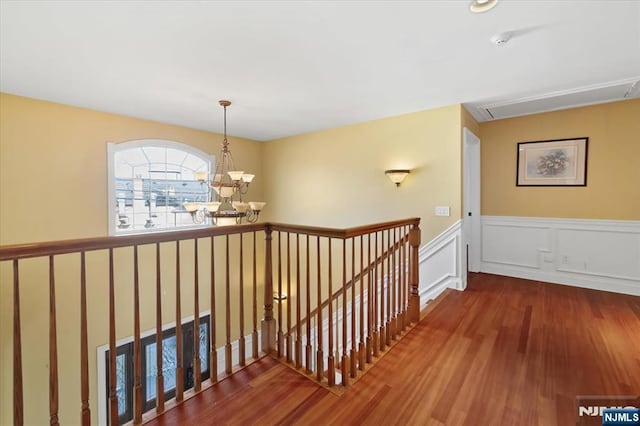 hallway with a wainscoted wall, an upstairs landing, wood finished floors, an inviting chandelier, and a decorative wall