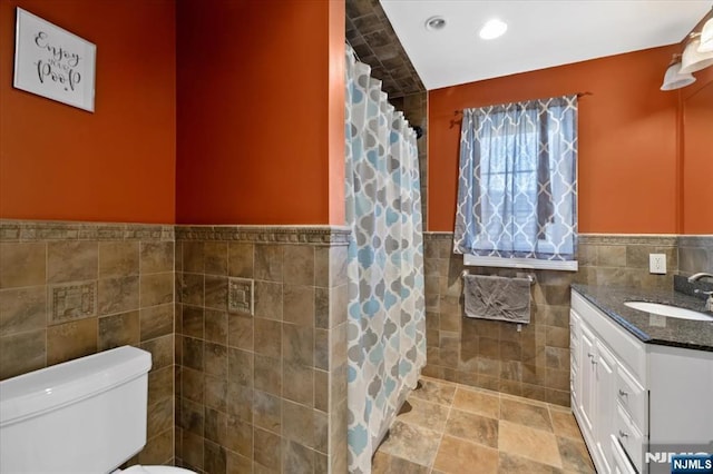 bathroom featuring vanity, recessed lighting, wainscoting, tile walls, and toilet