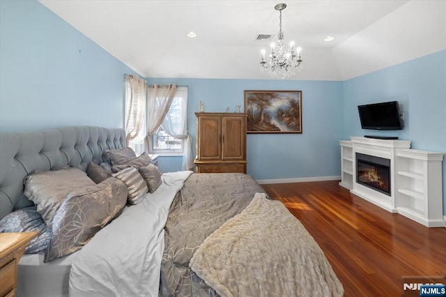 bedroom with visible vents, a glass covered fireplace, baseboards, dark wood-style flooring, and vaulted ceiling