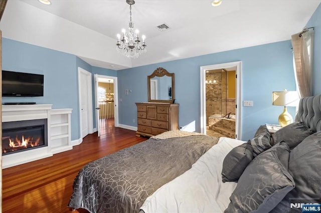 bedroom with wood finished floors, visible vents, baseboards, ensuite bath, and a glass covered fireplace