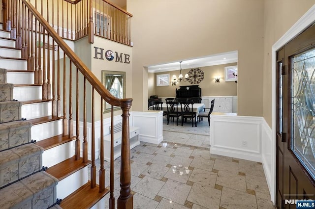 entrance foyer featuring a chandelier, stone tile floors, wainscoting, a towering ceiling, and a decorative wall