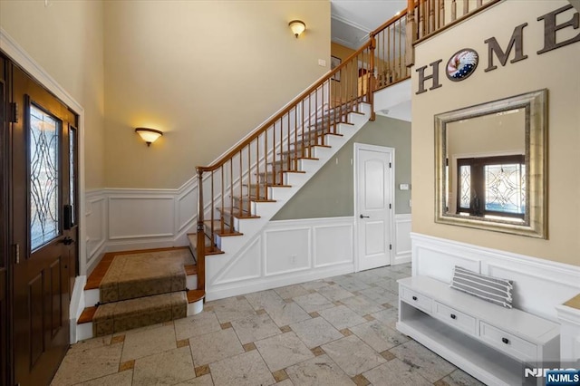 entryway featuring stairway, a wainscoted wall, a towering ceiling, and a decorative wall