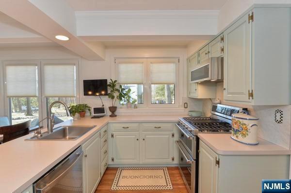 kitchen with sink, white cabinets, stainless steel appliances, crown molding, and light wood-type flooring