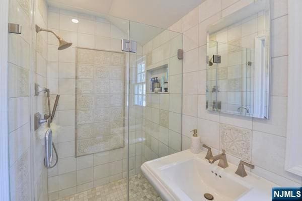 bathroom with a shower with door, sink, and tile walls