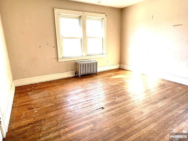 empty room featuring radiator heating unit and hardwood / wood-style flooring