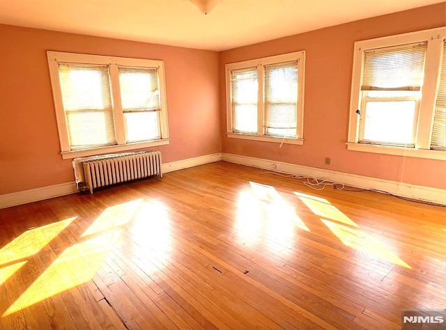 empty room featuring a wealth of natural light, radiator heating unit, and light wood-type flooring