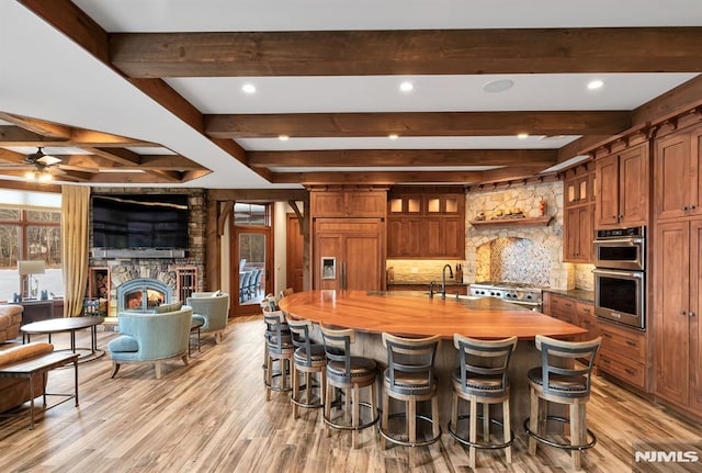 kitchen featuring a stone fireplace, backsplash, paneled built in refrigerator, range, and beam ceiling