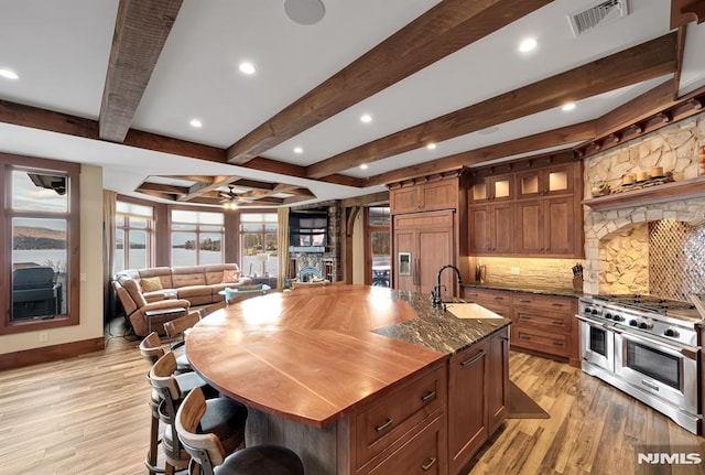 kitchen featuring high end appliances, sink, a kitchen island with sink, ceiling fan, and beam ceiling