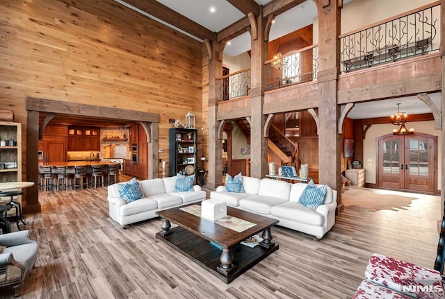 living room with an inviting chandelier, light hardwood / wood-style floors, a towering ceiling, and wooden walls