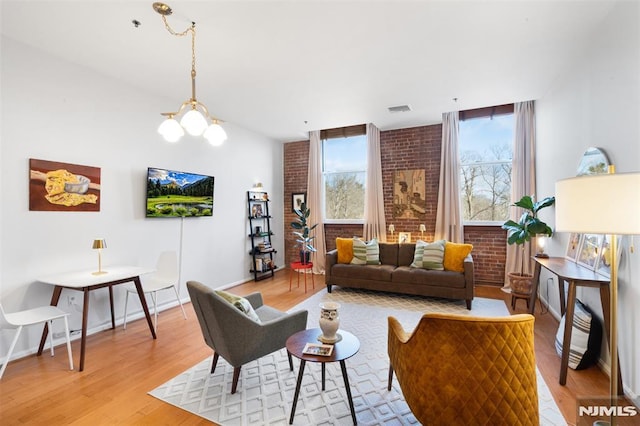 living room featuring brick wall, a chandelier, and light hardwood / wood-style flooring