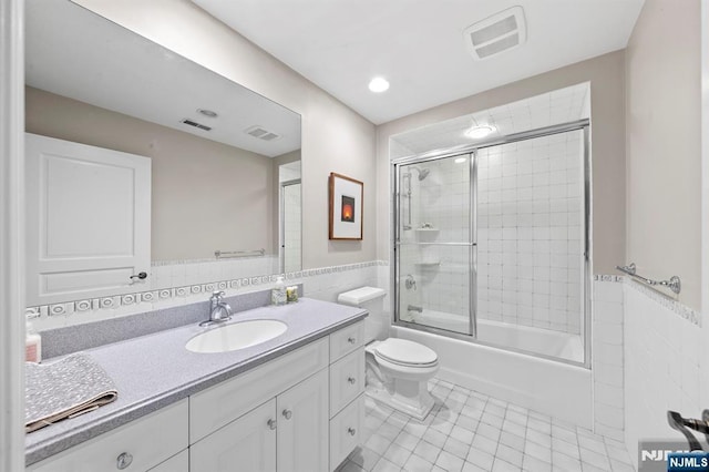 full bathroom featuring combined bath / shower with glass door, tile walls, tile patterned flooring, vanity, and toilet