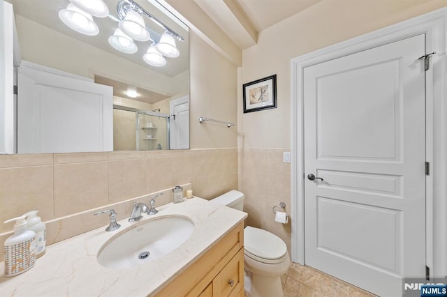 bathroom with toilet, tile walls, vanity, and a shower with shower door