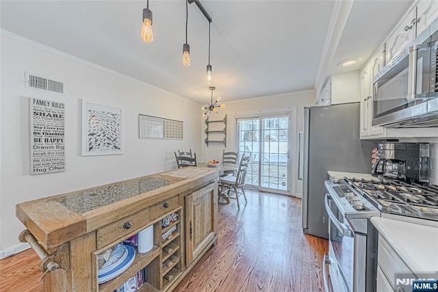 kitchen with dark wood-type flooring, appliances with stainless steel finishes, ornamental molding, white cabinets, and decorative light fixtures