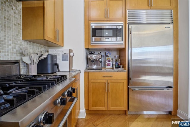 kitchen with built in appliances, backsplash, and light hardwood / wood-style floors