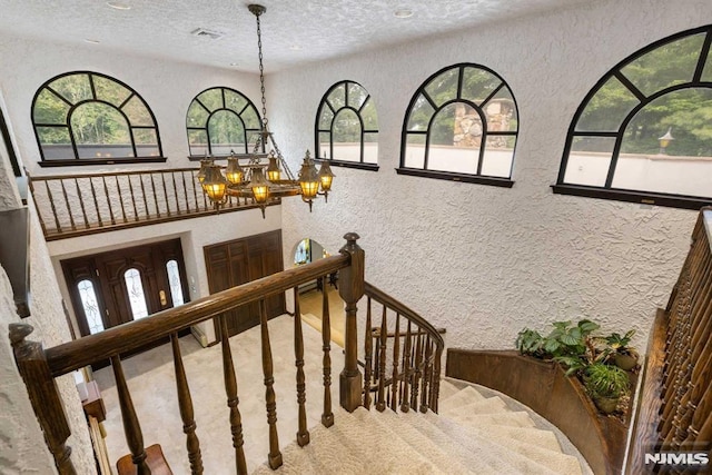 stairs featuring a textured ceiling, a wealth of natural light, and an inviting chandelier