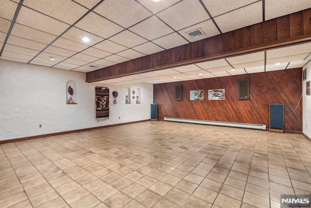 interior space featuring baseboard heating, wooden walls, and a drop ceiling