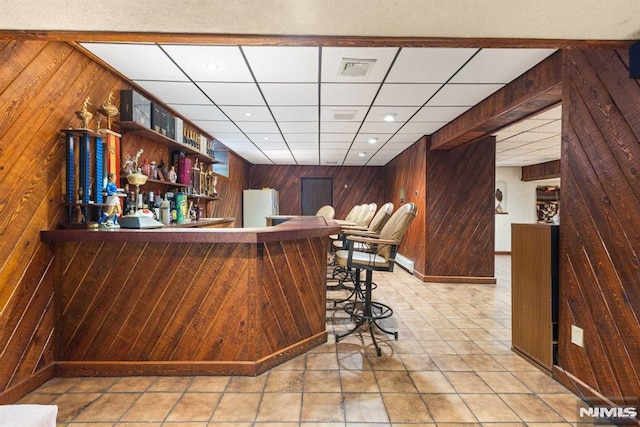 bar with a paneled ceiling, white fridge, and wooden walls