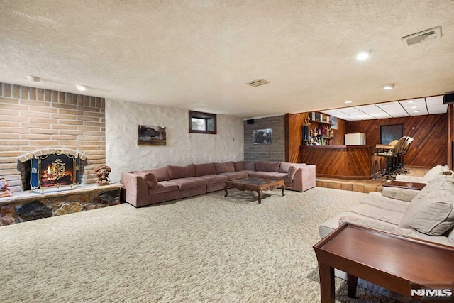 living room with a textured ceiling, wooden walls, carpet flooring, a brick fireplace, and bar area